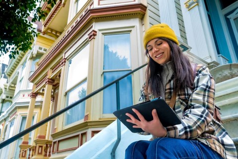 Young traveler woman sitting and smiling on steps outside a colorful victorian house in san