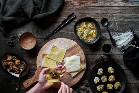 Top view of anonymous woman preparing wonton soup on a wooden table