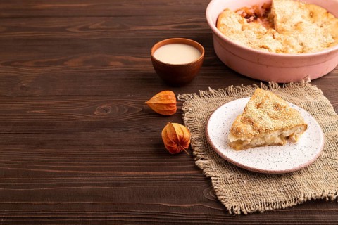 Apple Charlotte cake on brown wooden background and linen textile, cup of milk, side view, copy