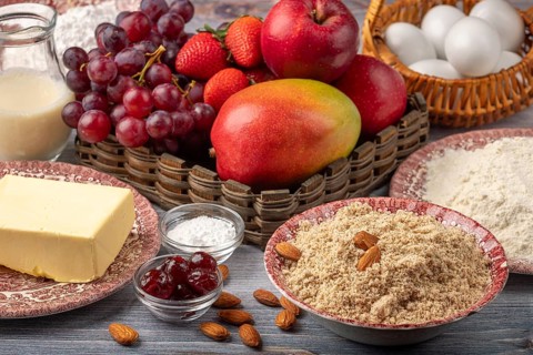 Ingredients for baking cake next to basket with grapes, apples, strawberries and mango