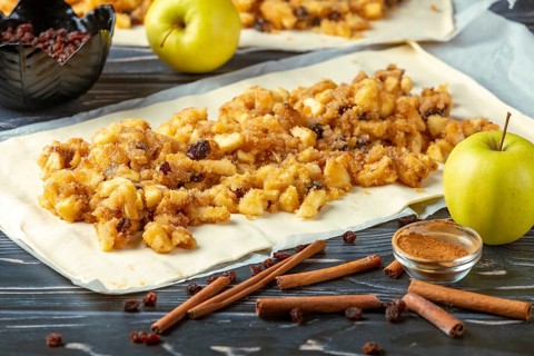 Rolled strudel dough with apple pieces, cinnamon and raisins