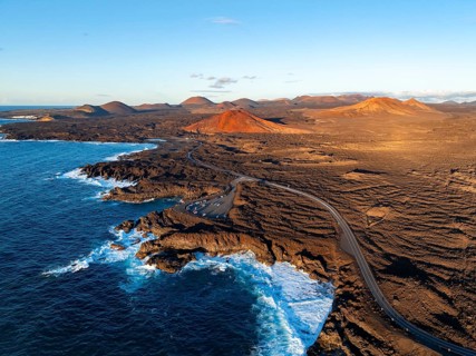Coast with lava fields, volcanic landscape near Los Hervideros with red volcano Montaña Bermeja, in