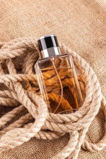 A sophisticated male perfume bottle nestled in a rustic rope set against a burlap background,