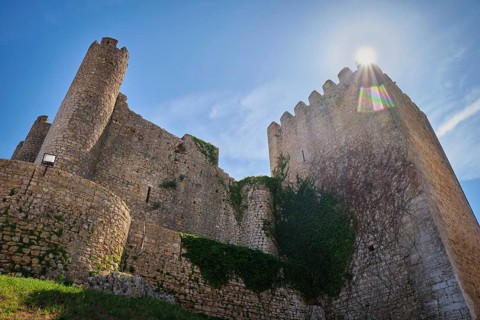 Low angle view of Obidos Castle in Obidos, Portugal, with massive stone towers, ivy covered walls