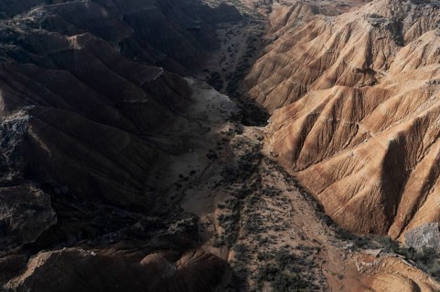 Aerial view of a rugged desert canyon with steep, eroded cliffs and a dry riverbed Shadows