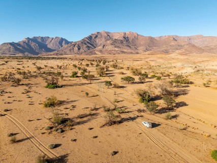 Aerial view of off-road car driving in dry riverbed and desert landscape on the Ugab River, behind