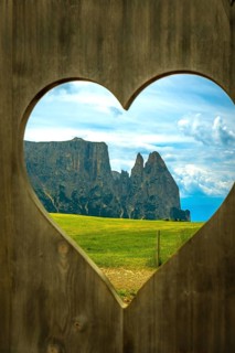 Breathtaking view of the dolomites mountains through a heart shaped opening in a wooden fence at