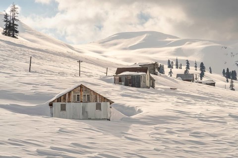 Rustic huts surrounded by pristine snow blanket a mountainous landscape in Georgia. The serene