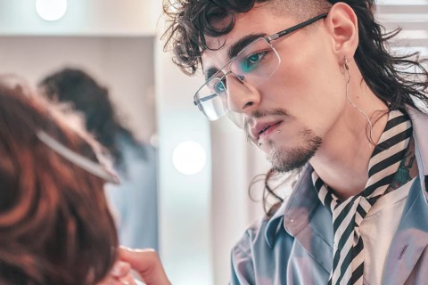 Skilled hairdresser with glasses, a mullet, and unique style is carefully styling a client's hair