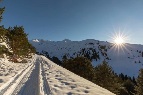 A scenic snowmobile trail winds through a serene snowy mountain landscape under a clear blue sky,