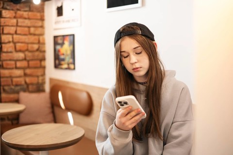 Teenage girl wearing casual clothing, intently focused on her smartphone while seated in a cozy