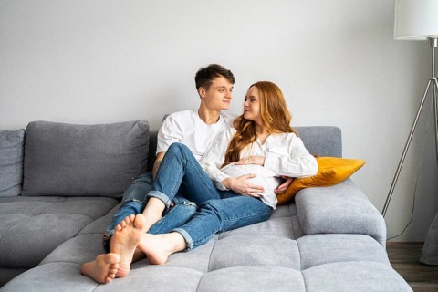 A young couple, expecting a baby, relaxes together on a cozy couch at home. The man and woman share
