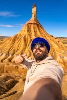 Tourist taking selfie and gesturing thumbs up in front of sandstone formation in bardenas reales
