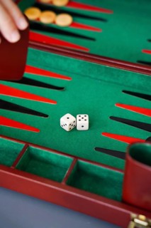 Close-up of a backgammon game with dice on a green board A hand holds the doubling cube, enhancing