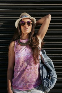 A stylish young woman wearing a straw hat, sunglasses, and a patterned top poses confidently