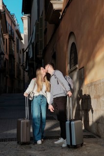 A young couple with luggage strolls through the charming, sunlit streets of Majorca, Spain,