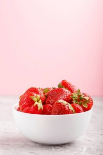 Fresh red strawberry in white bowl on gray and pink background. side view, close up, selective