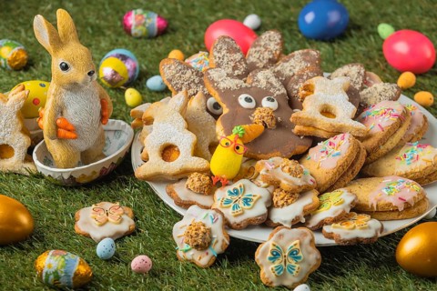 Decorated Easter cookies on a plate with a ceramic rabbit figurine and colorful eggs in the grass