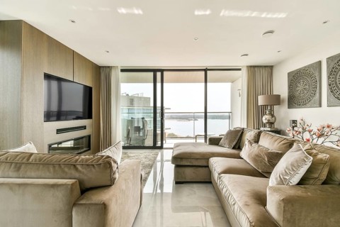 Elegant living room with large plush sofas facing a sleek wall-mounted TV. A glass door reveals a