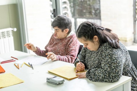 Two individuals at a mental health residence engage in creative activities. One is writing and the