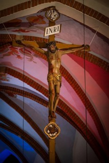 Traditional wooden crucifix with Jesus Christ inside a church with red and blue vaulted ceiling in