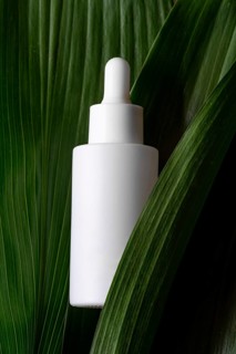 A sleek, white cosmetic dropper bottle elegantly positioned against a backdrop of lush green