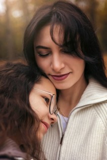 A tender moment between a mother and daughter in an autumn forest setting. They share a loving