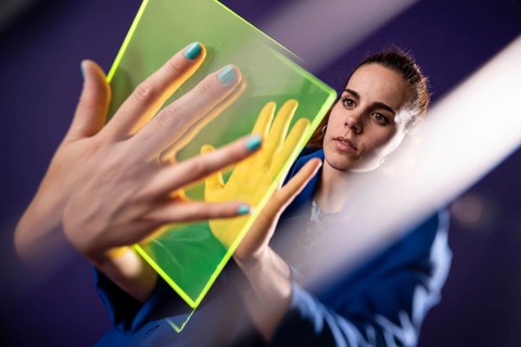 A young woman interacts with a futuristic device, exploring augmented reality. Her hands hover over