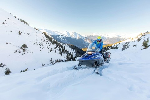 A snowmobiler navigates through pristine winter landscapes in the mountains, surrounded by
