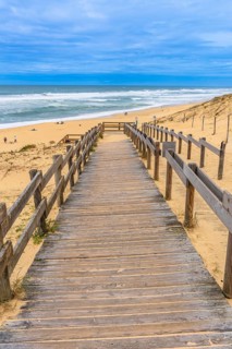 Wooden boardwalk leads down to sandy landes beach and atlantic waves under a clear blue sky, a