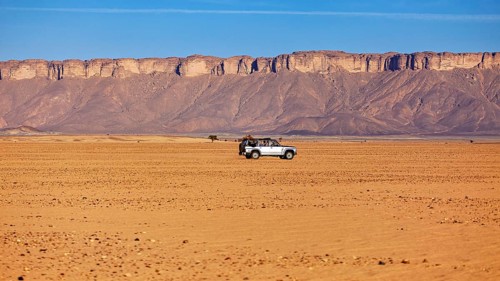 A lonely off-road vehicle in the vast, barren desert landscape with rock formations, By off-road