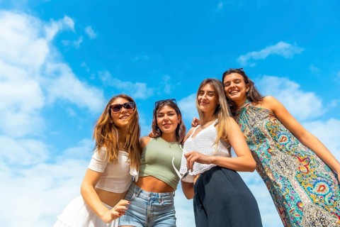 Four young women smiling and laughing together outdoors on a sunny day, enjoying friendship, summer