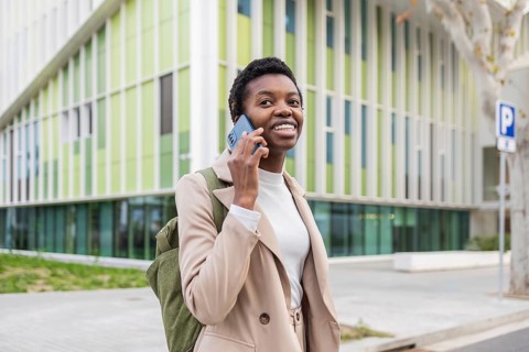 A stylish black woman confidently talks on her phone while walking in an urban environment She