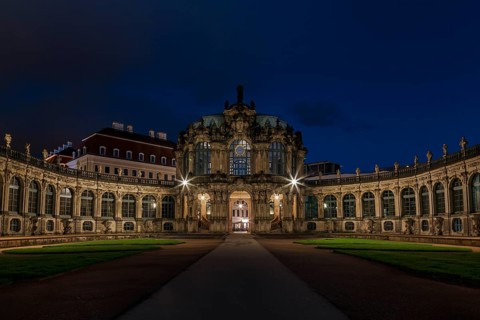 The Zwinger Palace in Dresden, Germany, is beautifully illuminated under a deep blue night sky.