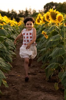 A young girl runs joyfully along a path in a lush sunflower field, her dress fluttering as she