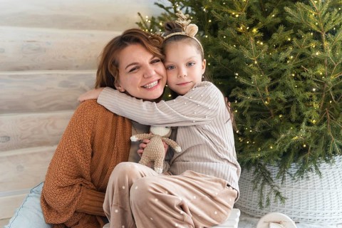 A joyful mother and her young daughter cuddling near a beautifully decorated Christmas tree. Both
