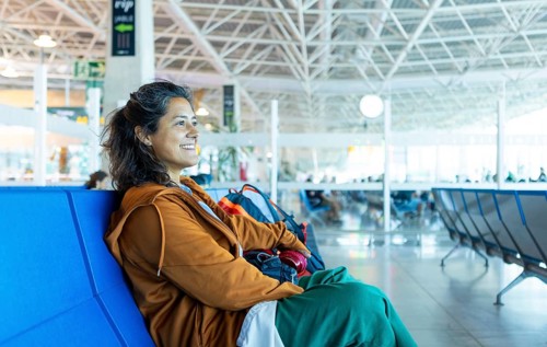 A woman sits contently on a bench in an airport terminal, exuding happiness and excitement Her
