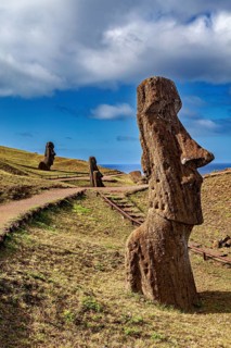 Close-up of a moai along a path with several statues under a blue sky, The moai statues on Easter
