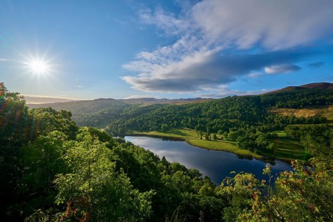 Brilliant sun over a green landscape with clouds and a lake, Queens View, Fincastle, Pitlochry,