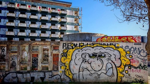 Wall with graffiti in front of urban building, hotel ruin, lost place in the background, blue sky