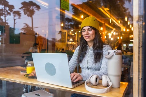 Young woman focused on laptop at a wooden table in a busy san francisco cafe, enjoying coffee and