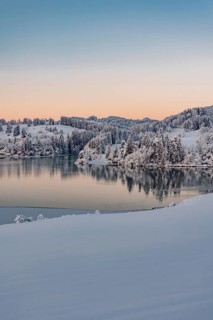 Dawn and sunrise at the wintry Forggensee in a snow-covered winter landscape in the foothills of