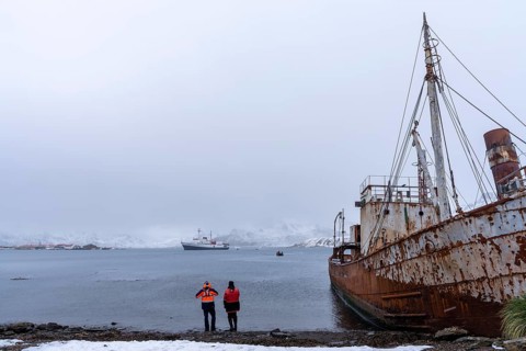 Rusted wreck of the whaling ship Petrel on the shore, two people in expedition clothes looking at