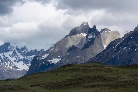 Cuernos del Paine, distinctive granite peaks with snowfields under cloudy sky, grassy steppe hills