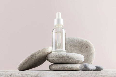 A minimalist composition featuring a dropper serum bottle balanced on smooth gray stones The serene