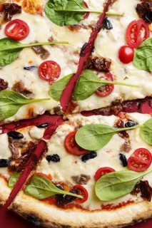 Close up view of a gourmet pizza with anchovies, sun-dried tomatoes, cranberries, cherry tomatoes,