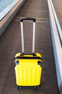 A vibrant yellow suitcase sits on an airport conveyor belt, highlighting the theme of travel and