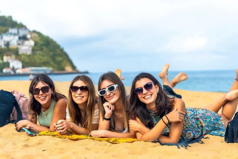 Four happy young women friends lying on a towel enjoying summer vacation on a sandy beach, having