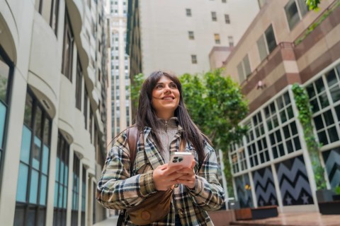 Young woman walking downtown san francisco, smiling and using smartphone to navigate and explore