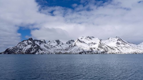 Snow-capped mountain range with rugged peaks seen from the sea, cloudy sky over the South Atlantic,